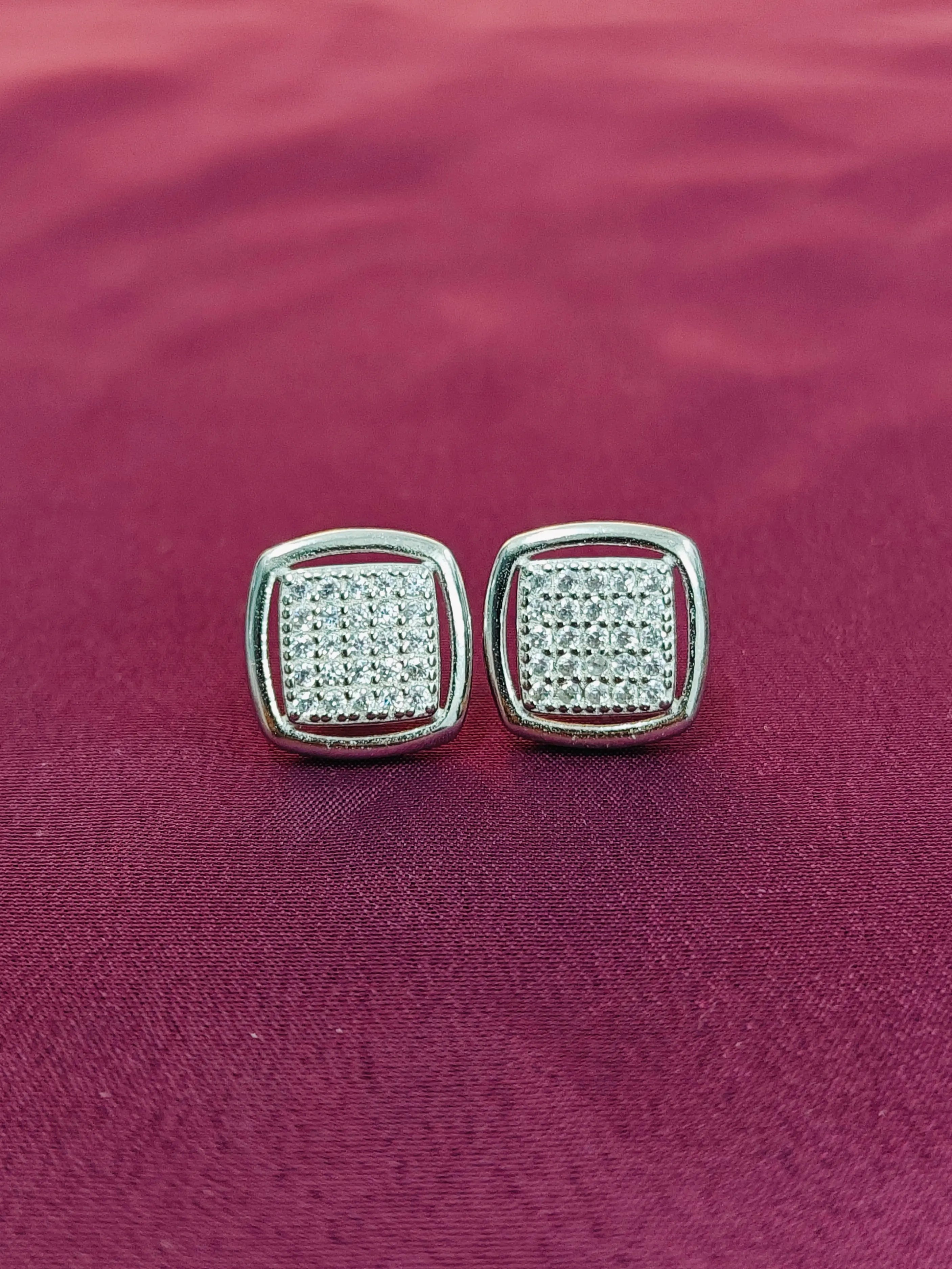 Pair of silver square earrings with clear stones on a purple fabric background